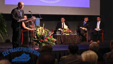 Eli Capilouto speaks at a podium with Bill Gatton listening